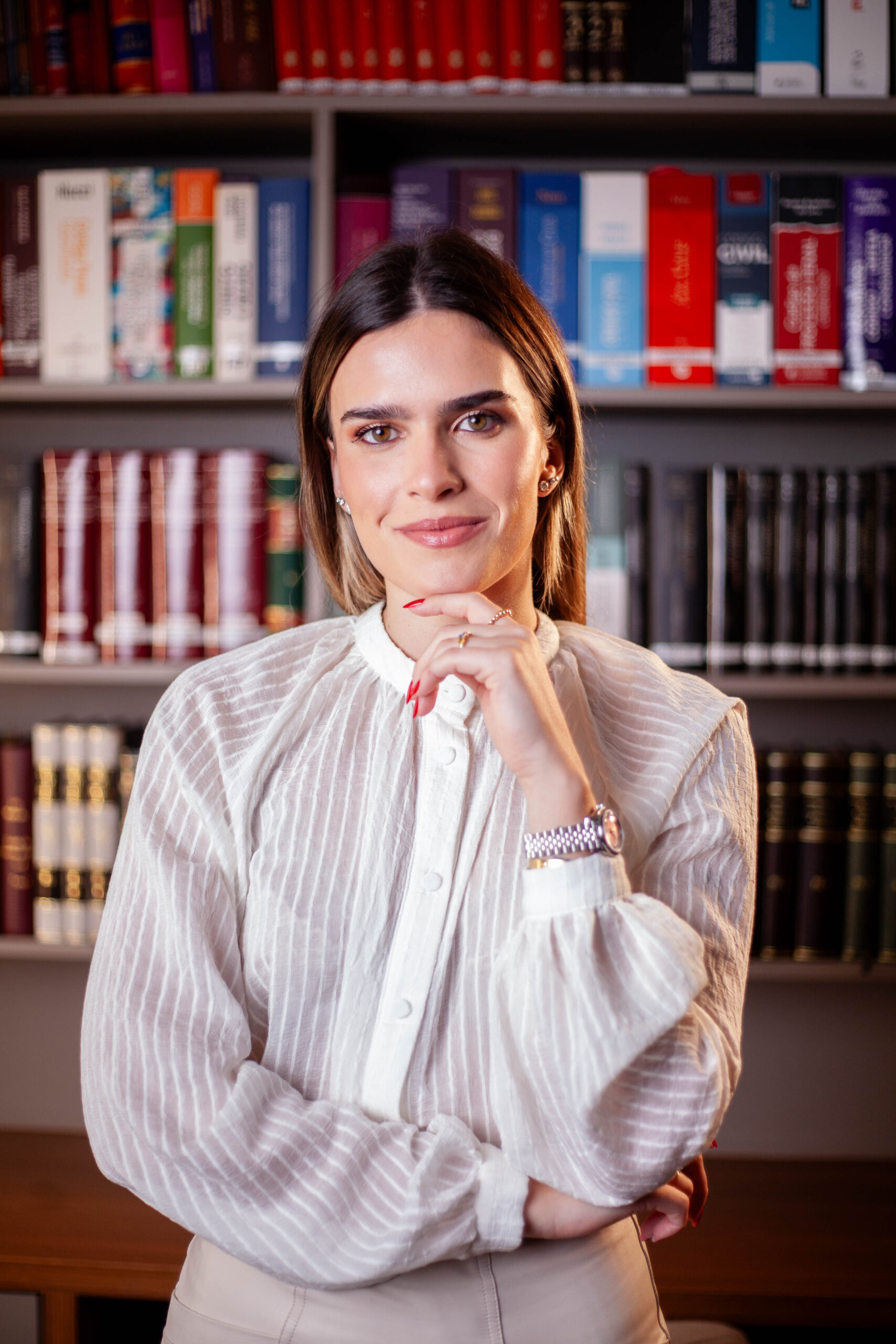 Advogada Maria Gois, da Gois Advogados, vestindo camisa social clara, posando em frente a uma estante de livros jurídicos.